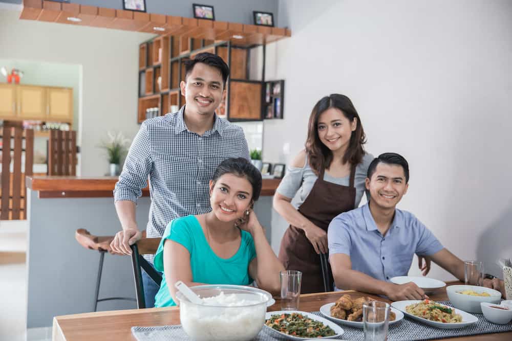 Four people sharing a meal together at a dining table set with various dishes in a modern kitchen, symbolizing the benefits of organic foods in promoting healthier diets.