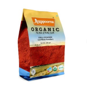 Annapoorna Organic Chilli Powder packaging, predominantly yellow with a landscape image transitioning into a deep red color representing the chili powder. The package indicates it as a 100 grams organic product with the tagline 'The Pride of Mother Earth' and USDA Organic and India Organic certification logos.