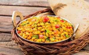 Image of a traditional Indian dish, Chana Masala, garnished with fresh tomatoes and herbs, served with Indian flatbread, as featured on the 'Kidney Bean Curry' page.