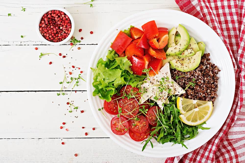 Image of a vibrant Quinoa Tofu Salad with fresh lettuce, sliced avocado, ripe tomatoes, a wedge of lemon, arugula leaves, and thinly sliced cheese, presented on a white plate on a checkered napkin, as featured on the 'Quinoa Tofu Salad' page.